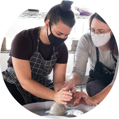 Two people enjoying a Vancouver pottery date night workshop, learning wheel-throwing techniques in a hands-on ceramics studio experience.