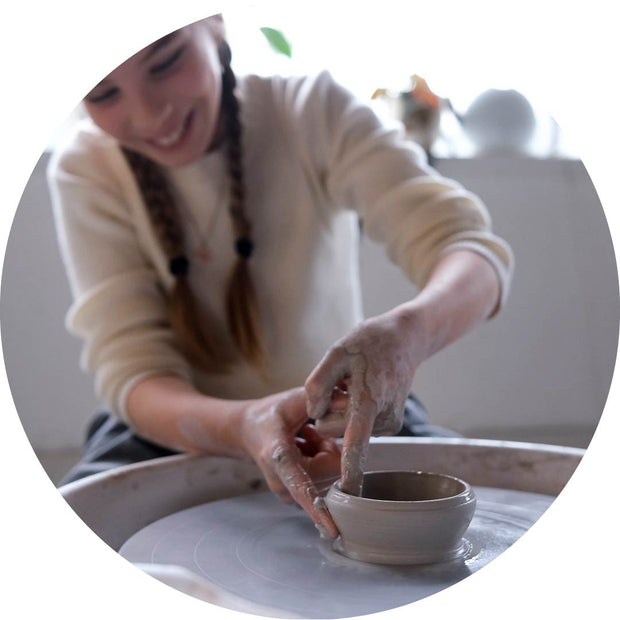 A smiling young girl learning wheel throwing in a Vancouver pottery youth class, shaping clay on a pottery wheel in a bright, welcoming studio. Perfect for beginner ceramic enthusiasts ages 10-16.