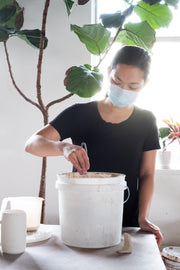 A student in a Vancouver ceramic glaze workshop mixing glaze in a large bucket, preparing it for application on pottery. This hands-on Vancouver pottery class teaches the chemistry behind ceramic glazes and how to create custom finishes for ceramic pieces.